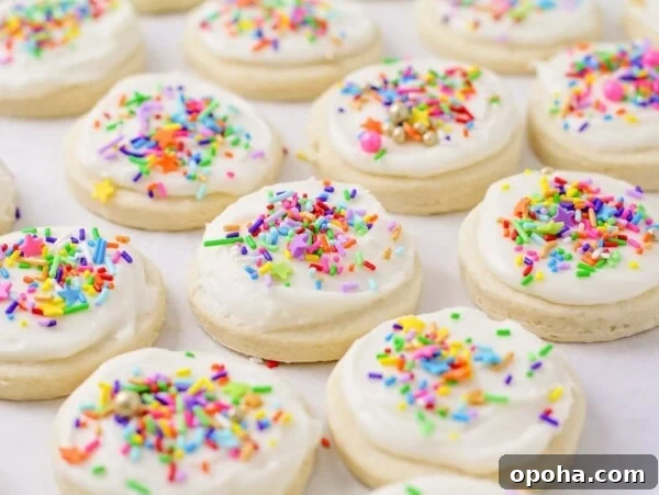 Frosted sugar cookies on parchment paper with sprinkles on top.