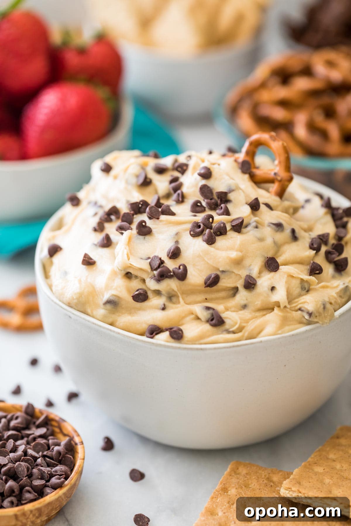 bowl of cookie dough dip topped with mini chocolate chips and a pretzel