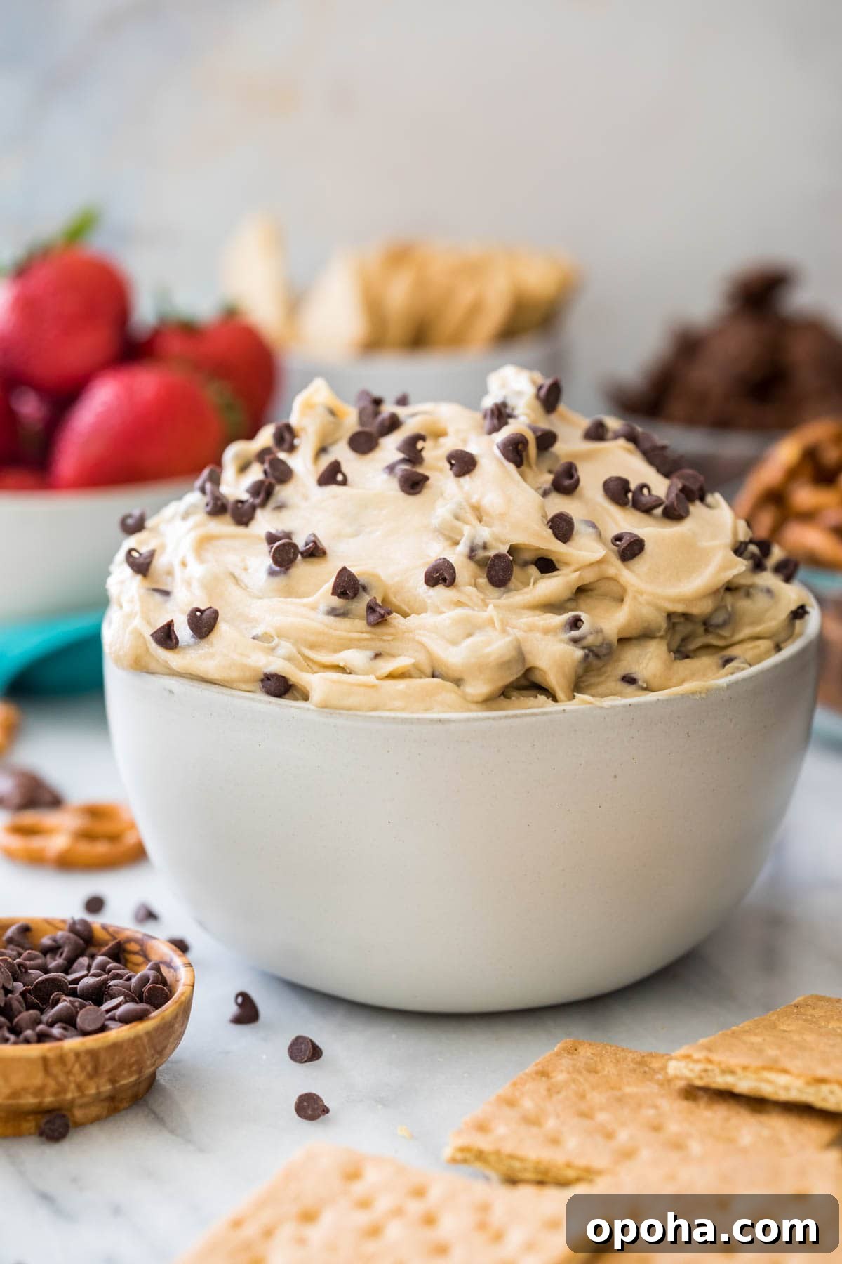bowl of cookie dough dip with bowls of strawberries, graham crackers, and teddy grahams in the background