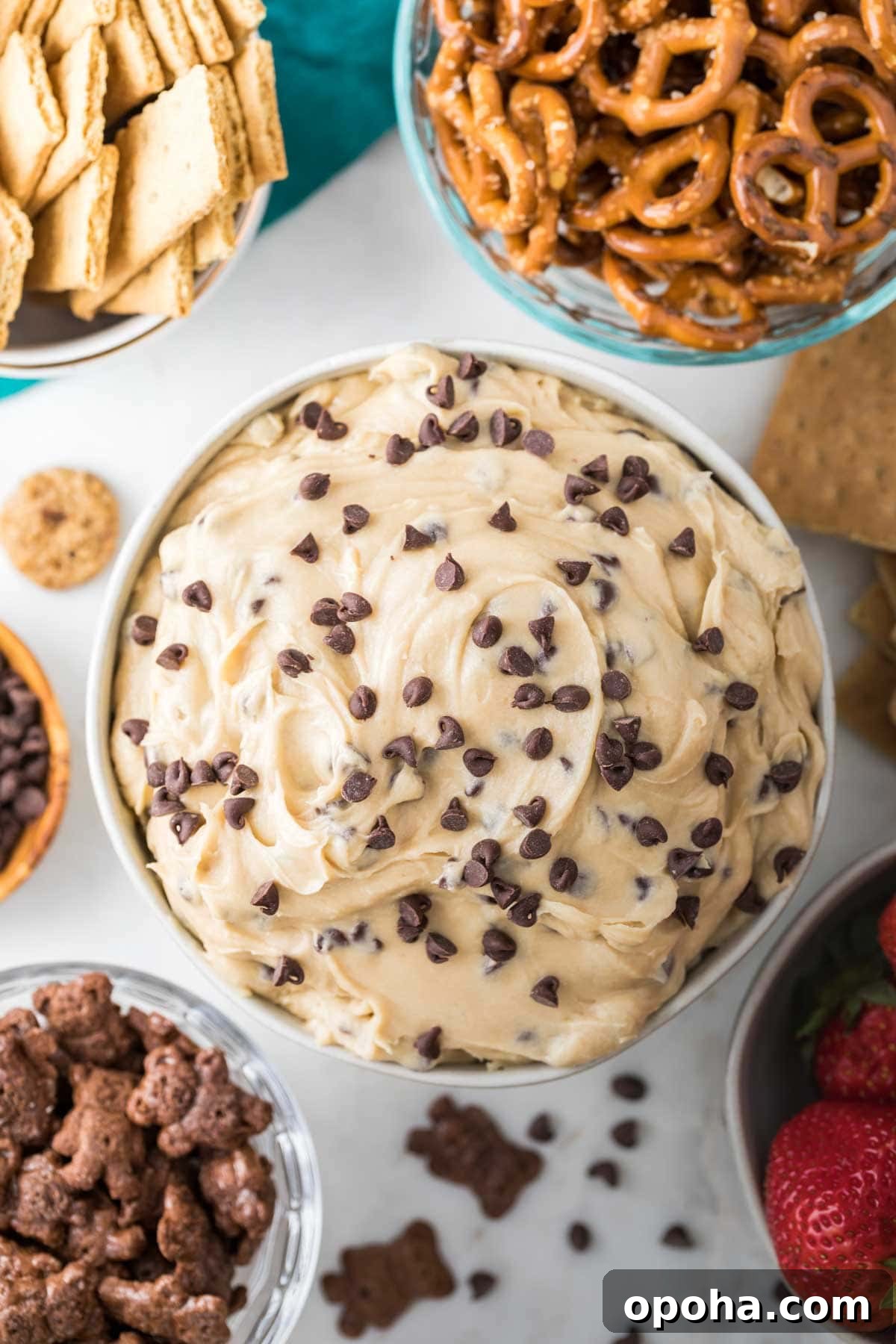 overhead view of cookie dough dip in bowl surrounded by bowls of pretzels, graham crackers, and teddy grahams