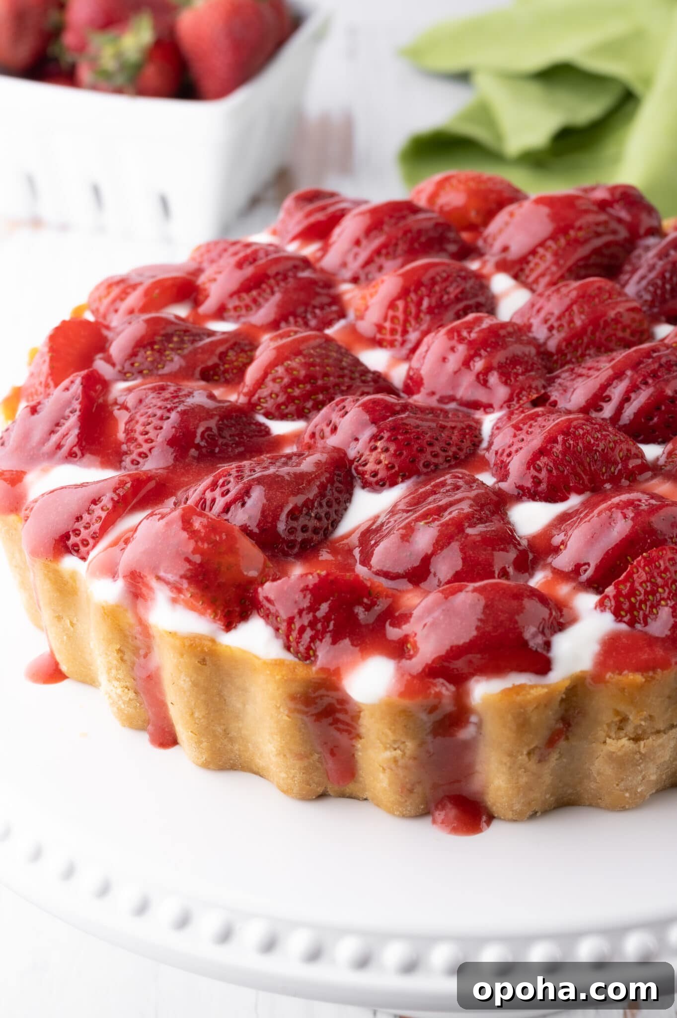 Keto strawberry cheesecake with fresh strawberries and drizzled with strawberry sauce.  The cheesecake rests on a bright white cake stand. 