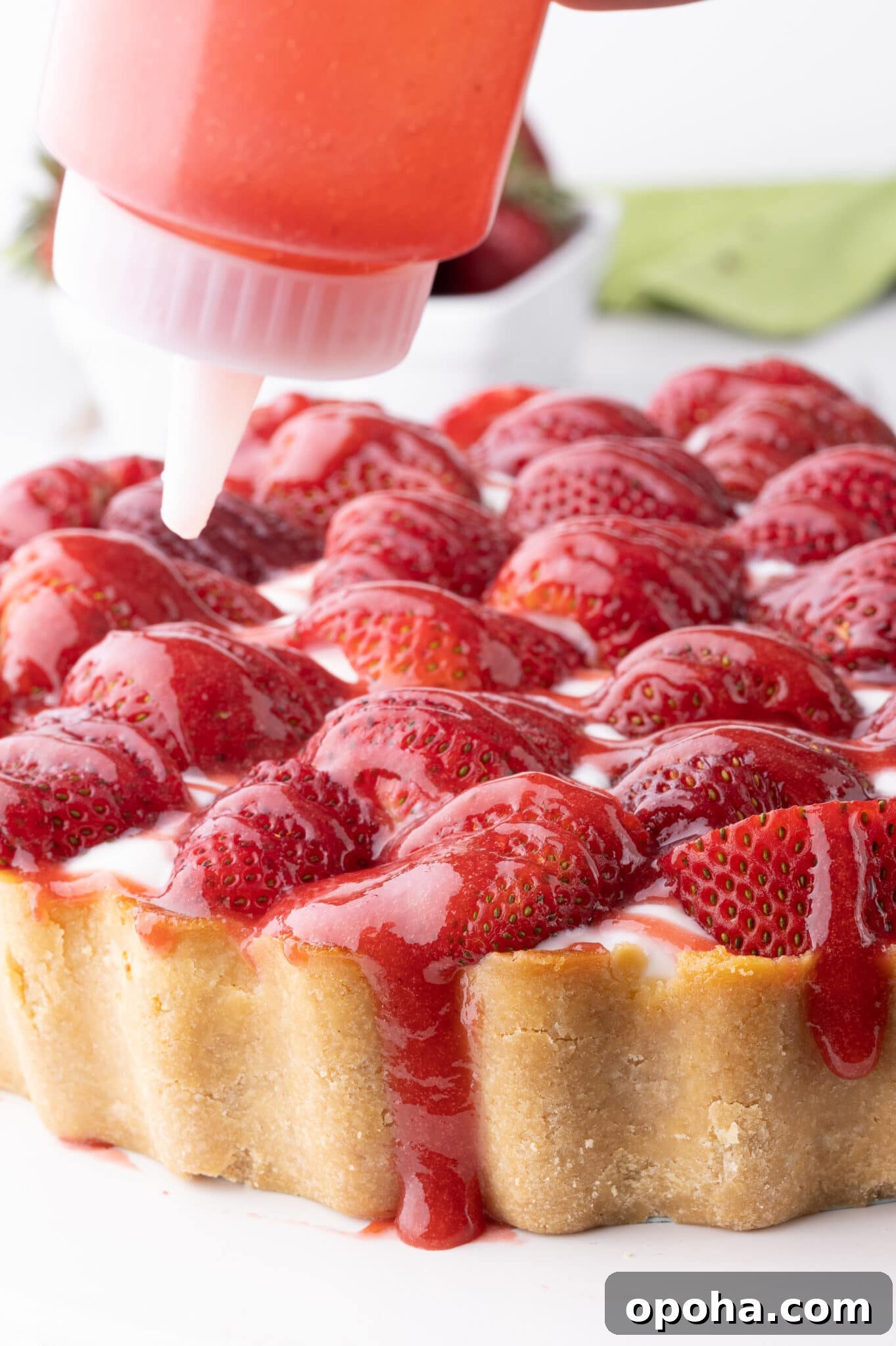 Strawberry sauce being squeezed from a condiment bottle onto our keto strawberry cheesecake.