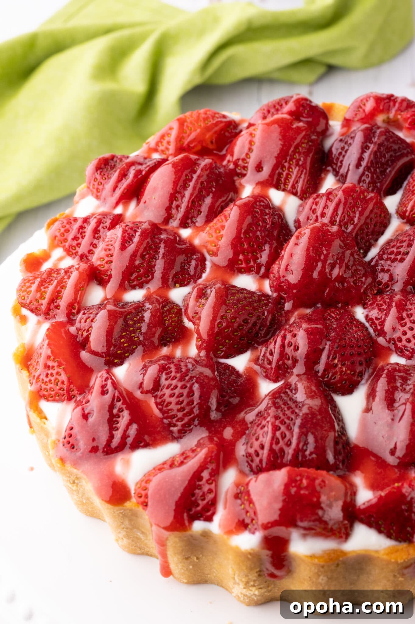 Keto strawberry cheesecake with fresh strawberries and drizzled with strawberry sauce.  The cheesecake rests on a bright white cake stand. 