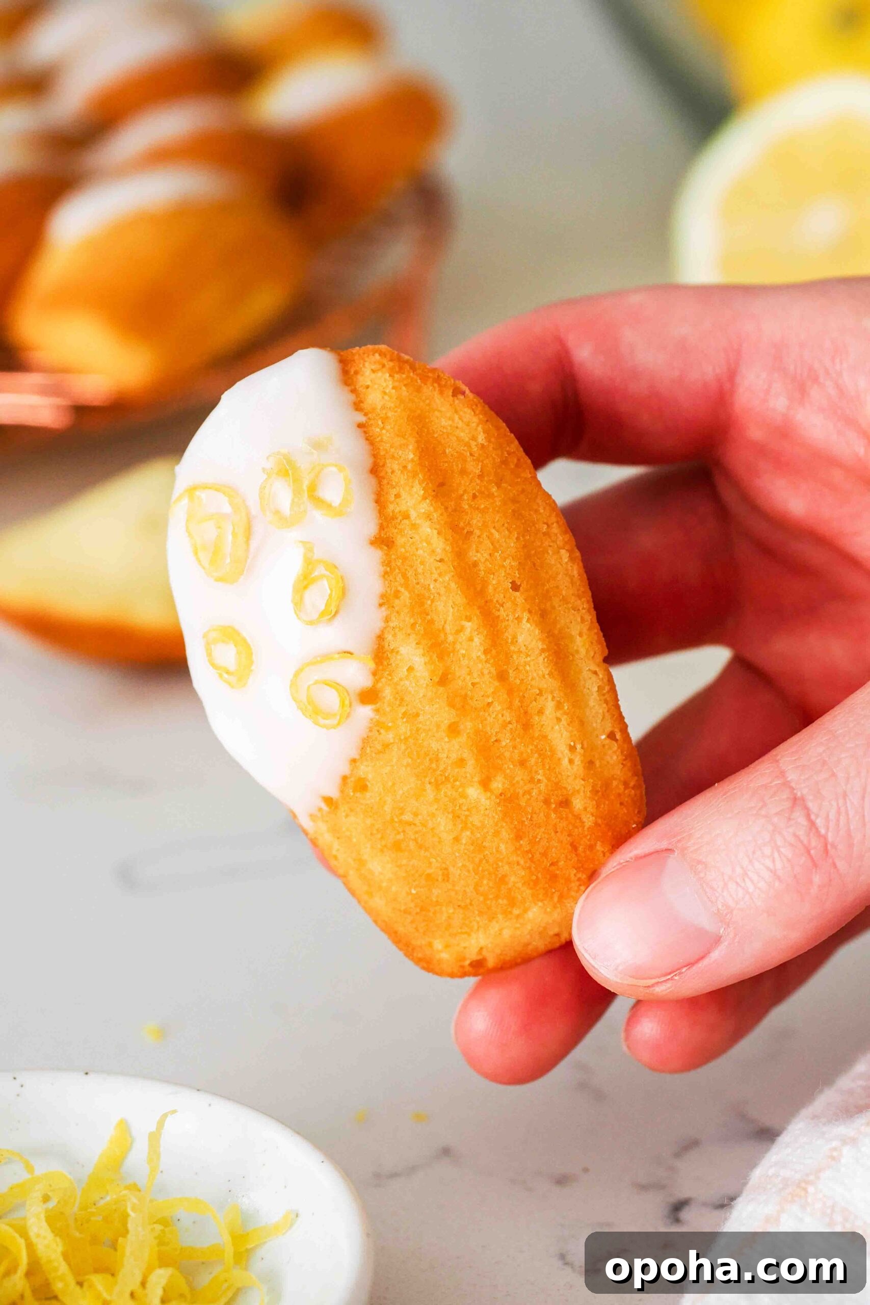 Zesty Lemon Madeleines: Classic French Tea Cakes Recipe 2 A hand holds up a glazed lemon madeleine.