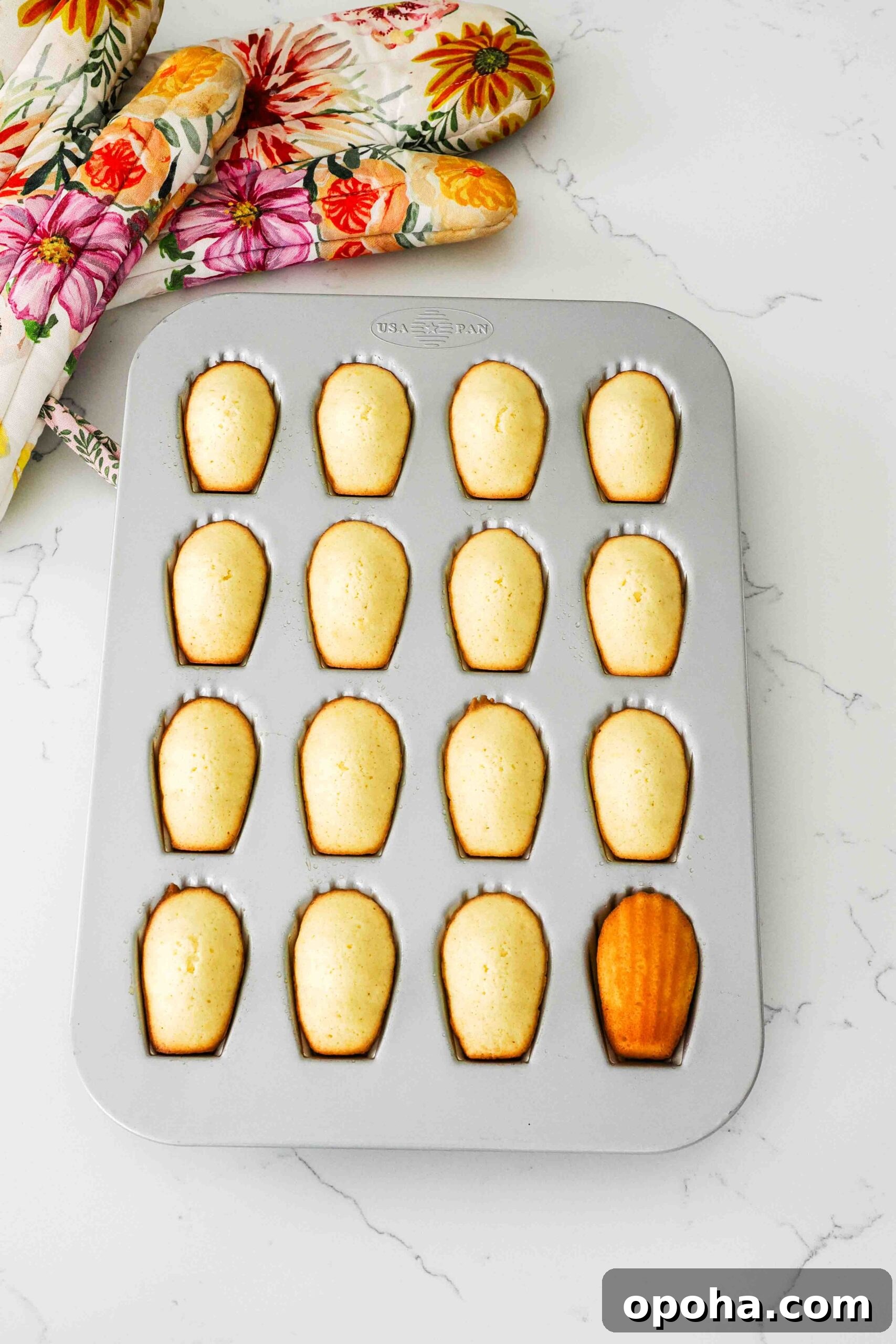 Zesty Lemon Madeleines: Classic French Tea Cakes Recipe 13 Baked lemon madeleines in a pan, with one flipped over to show a golden brown back.
