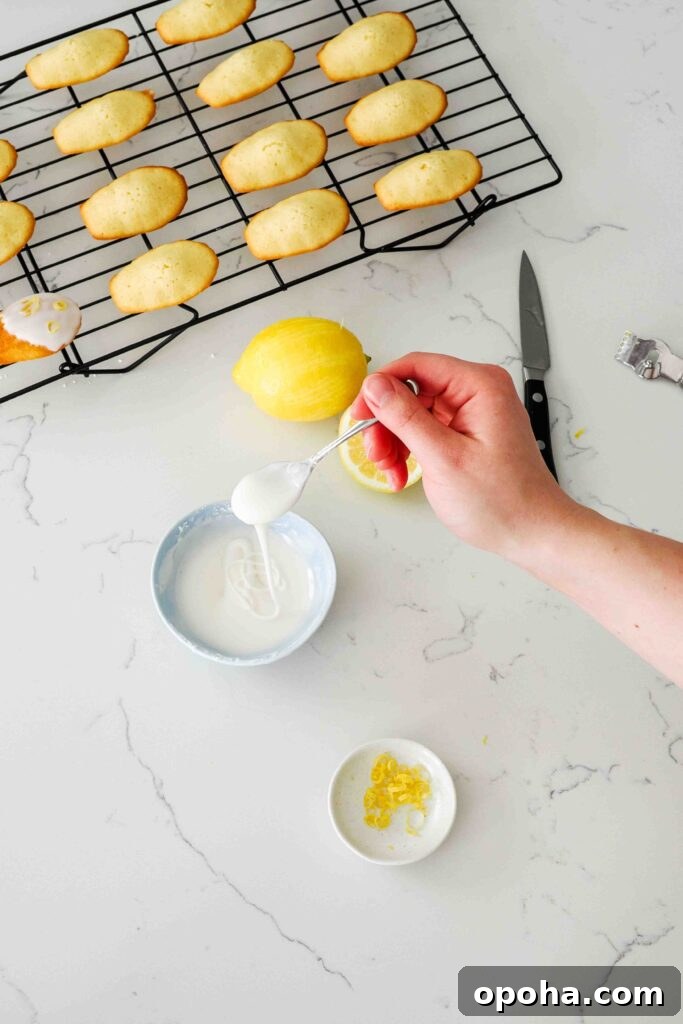 Zesty Lemon Madeleines: Classic French Tea Cakes Recipe 14 A spoon drizzles thick powdered sugar icing back into a bowl.