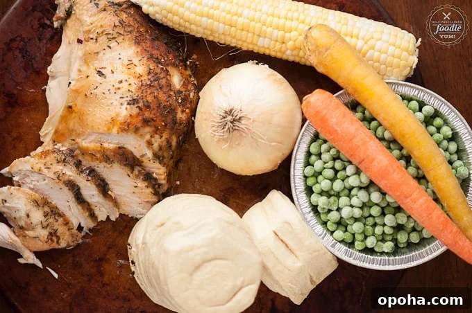 cooked turkey breast, onion, biscuit dough, corn cob, peas, carrot sticks on cutting board