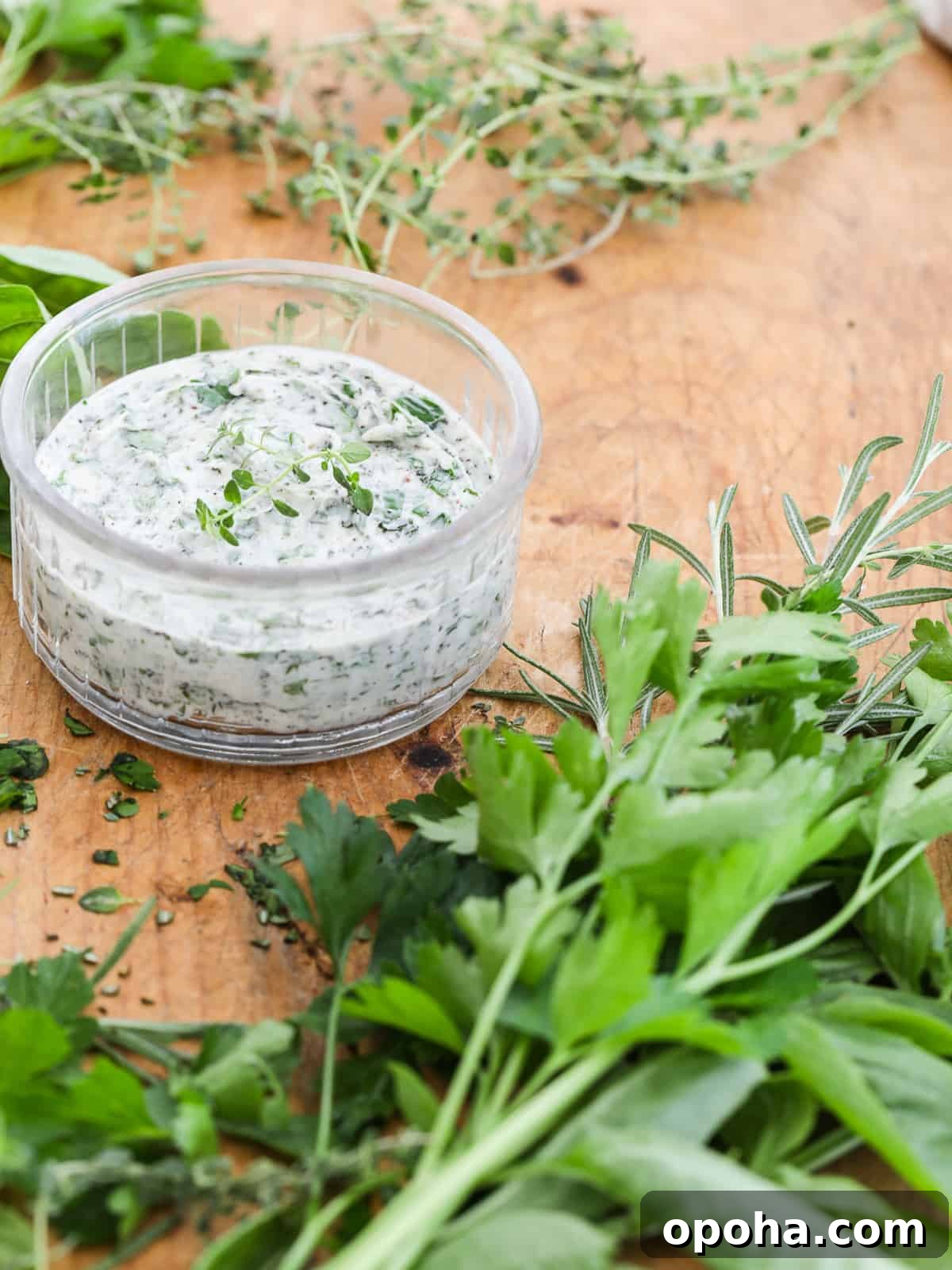 A clear round small dish filled with herb butter and herbs chopped on a cutting board.