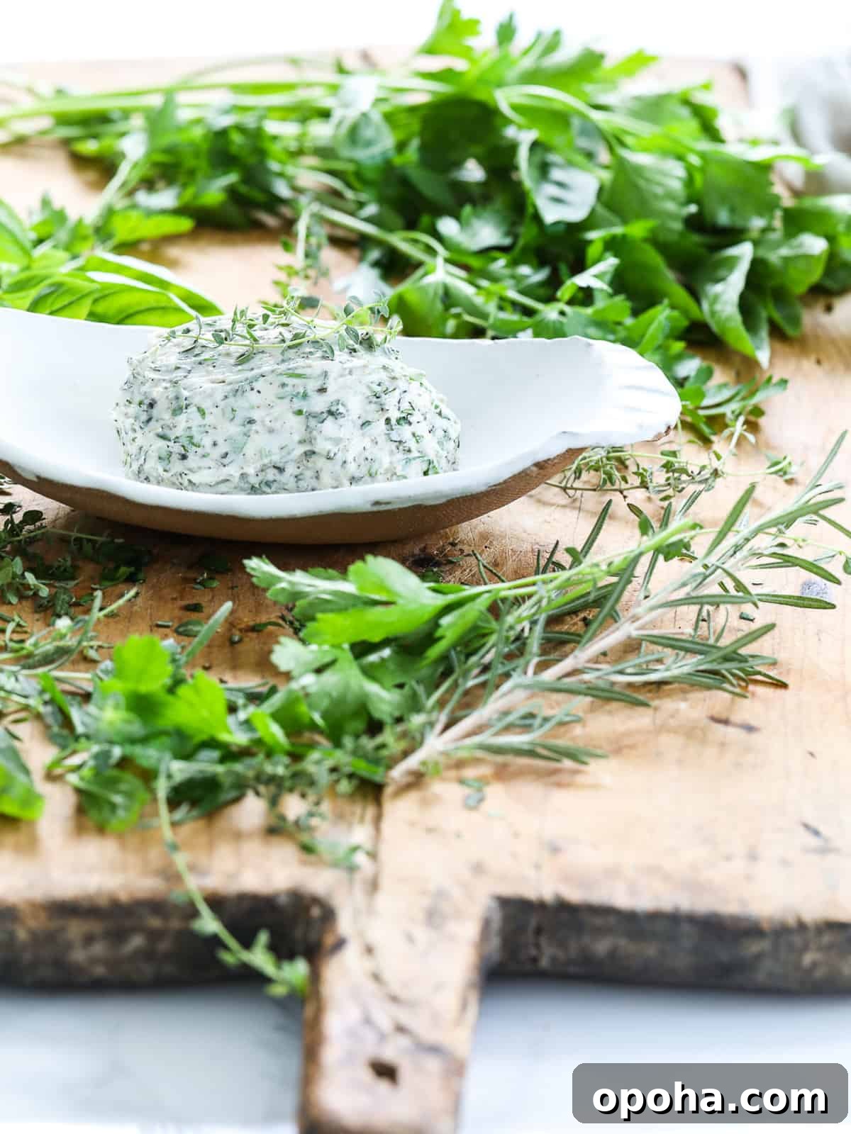 A white ceramic dish homemade herb butter and fresh herbs on a cutting board.