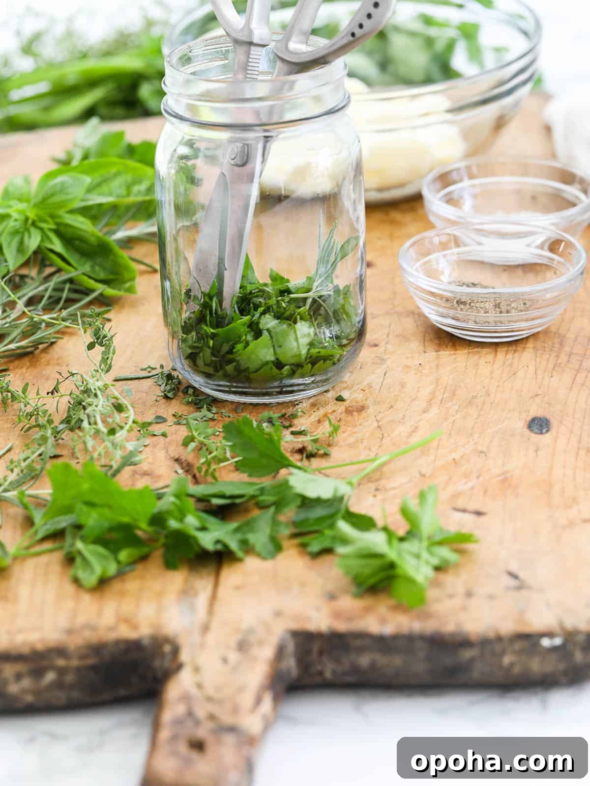 A pair of silver kitchen scissors in a glass jar with fresh herbs and butter to making herb butter.