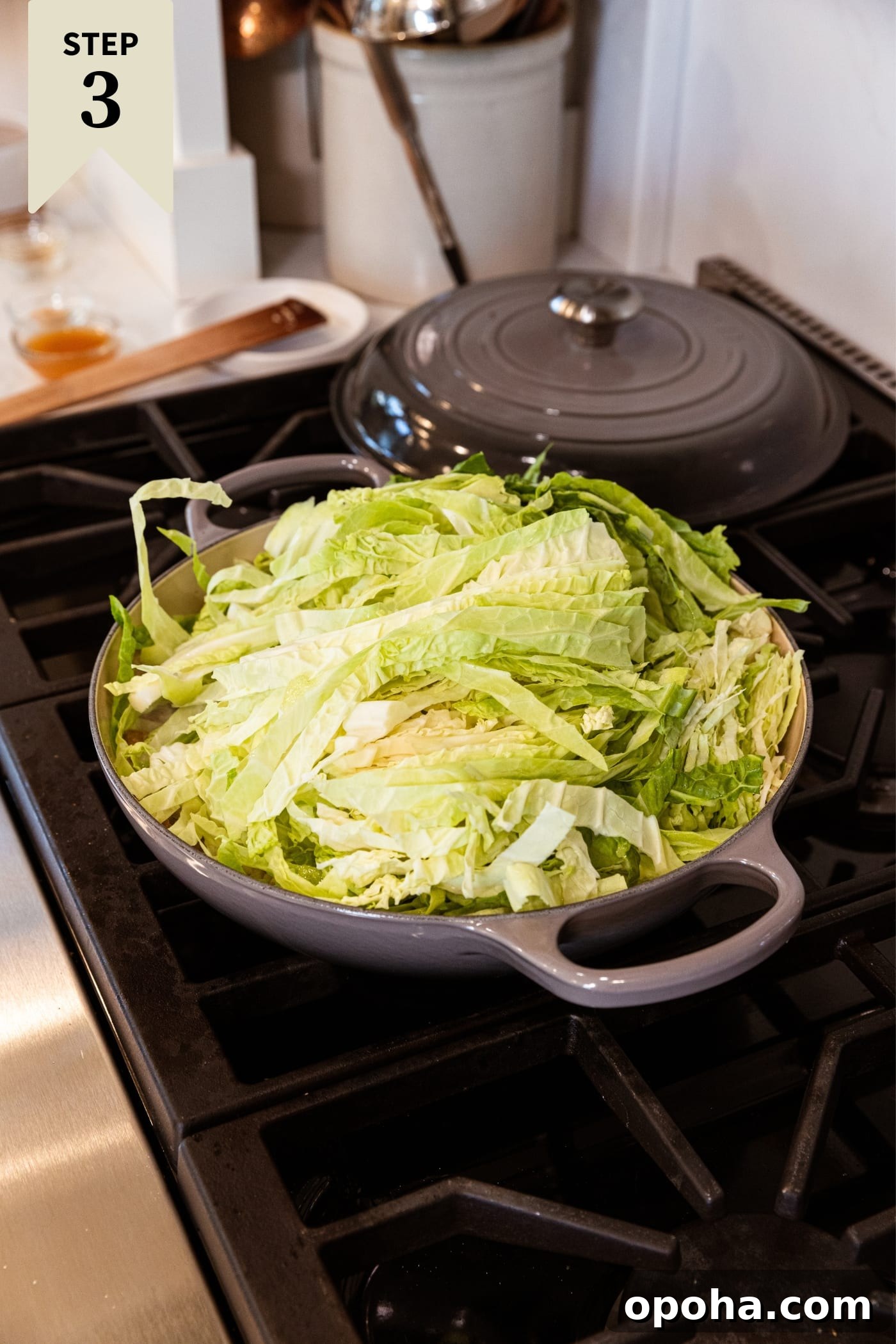 One-Pan Skillet Cabbage with Sausage and Garlic Butter 9 Large gray skillet on stovetop with lots of sliced cabbage beginning to wilt.