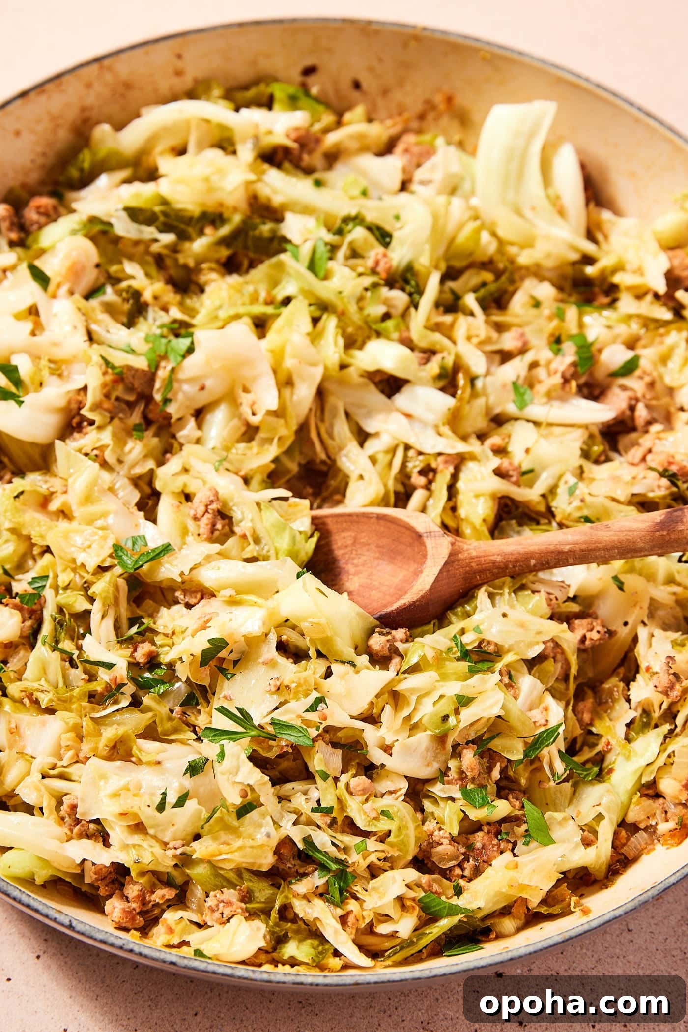 One-Pan Skillet Cabbage with Sausage and Garlic Butter 11 Large gray skillet filled with cooked cabbage and sausage with wooden spoon resting in pan.