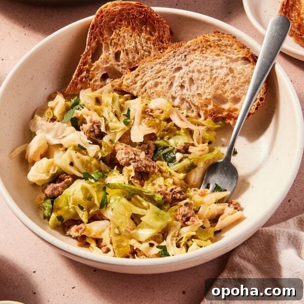 One-Pan Skillet Cabbage with Sausage and Garlic Butter 13 Large white bowl filled with serving of skillet sausage and cabbage with slices of toasted bread also in bowl with fork picking up a bite of cabbage.