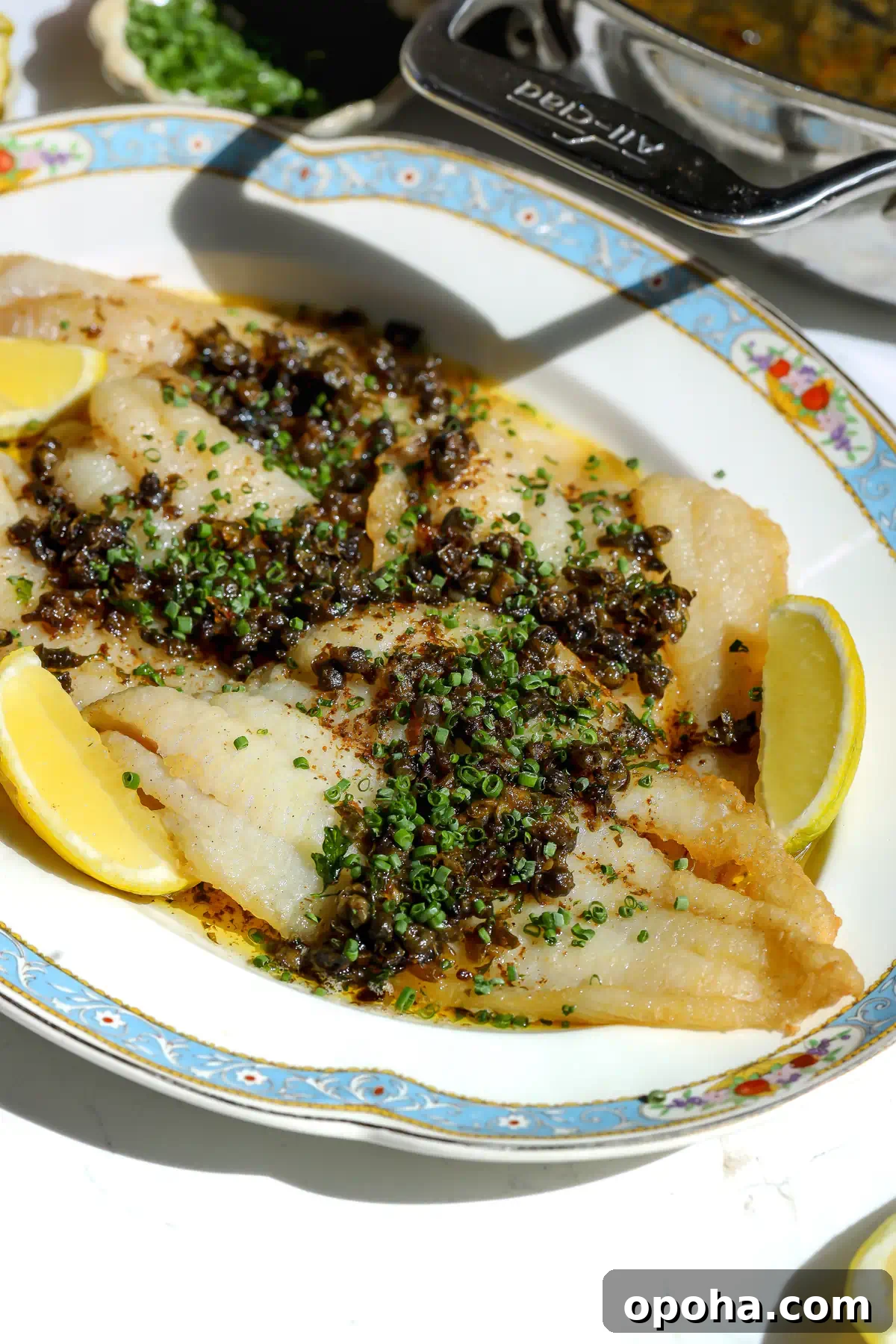 A close-up of a petrale sole meunière recipe featuring tender fish fillets topped with a browned butter and caper sauce on a pretty plate.