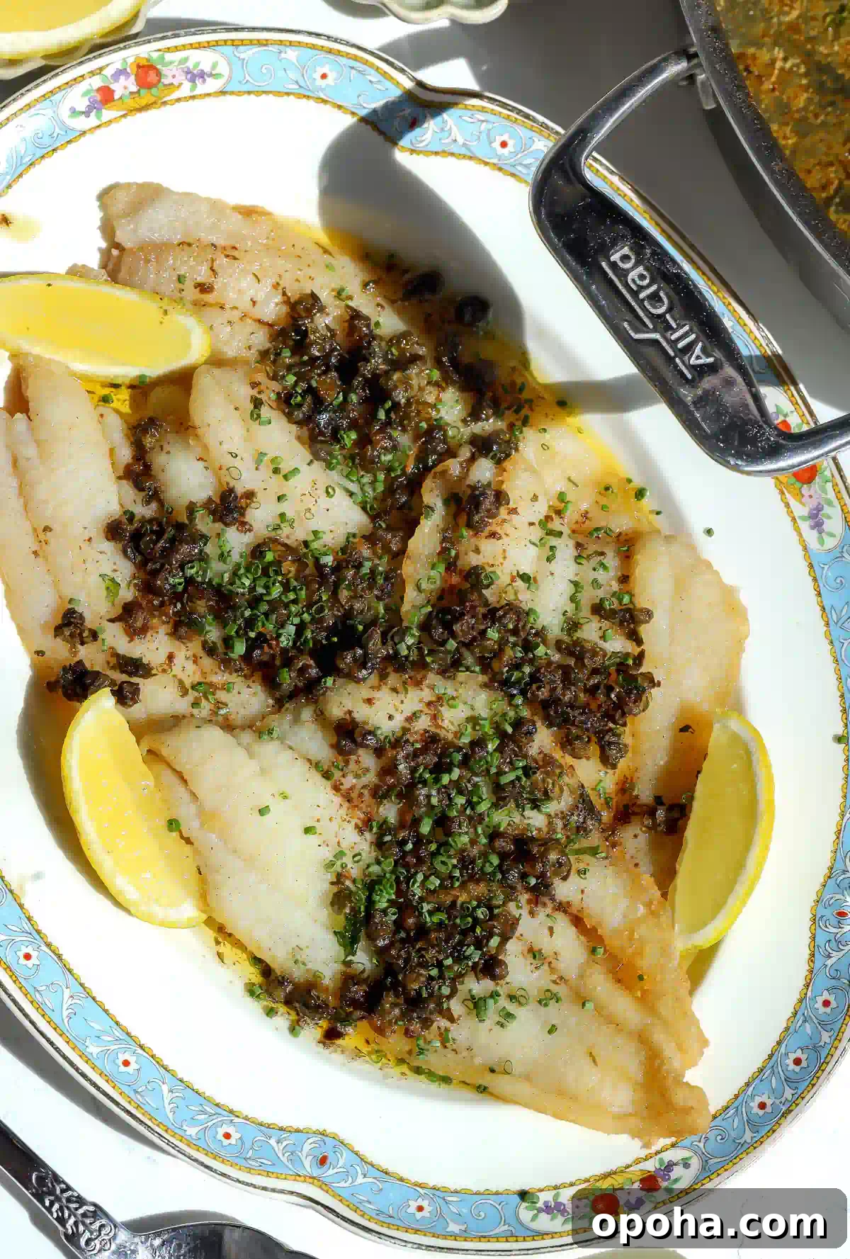 Overhead shot of freshly cooked petrale sole meunière garnished with chives and served with lemon wedges.