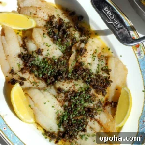 Overhead shot of freshly cooked petrale sole meunière garnished with chives and served with lemon wedges.