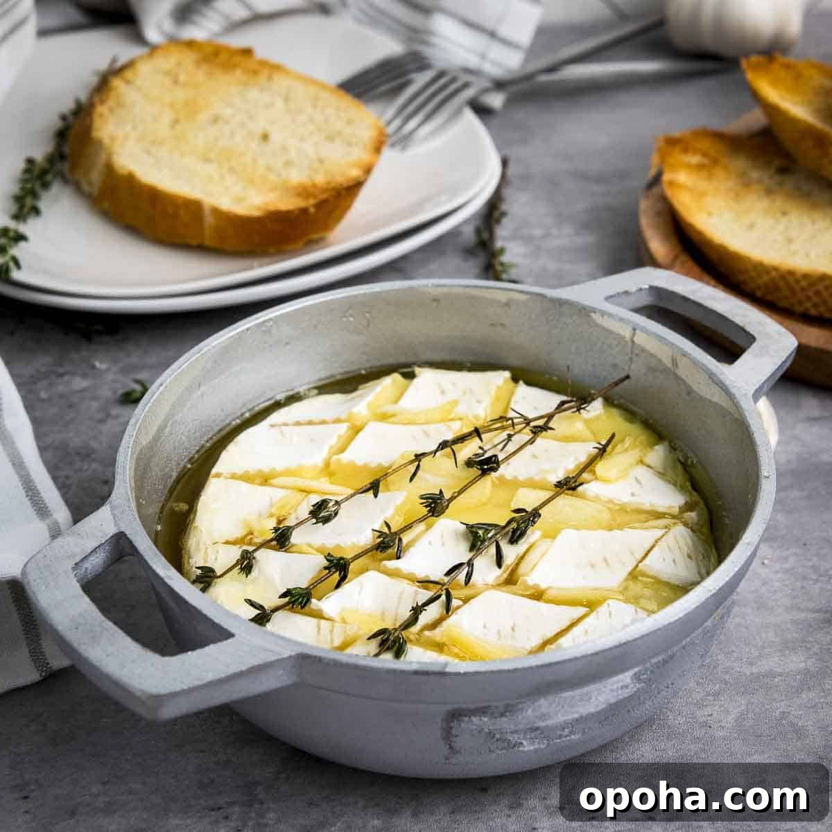 Side shot of baked brie garnished with fresh thyme in a small baking dish with more thyme sprigs and toasted bread on the side.