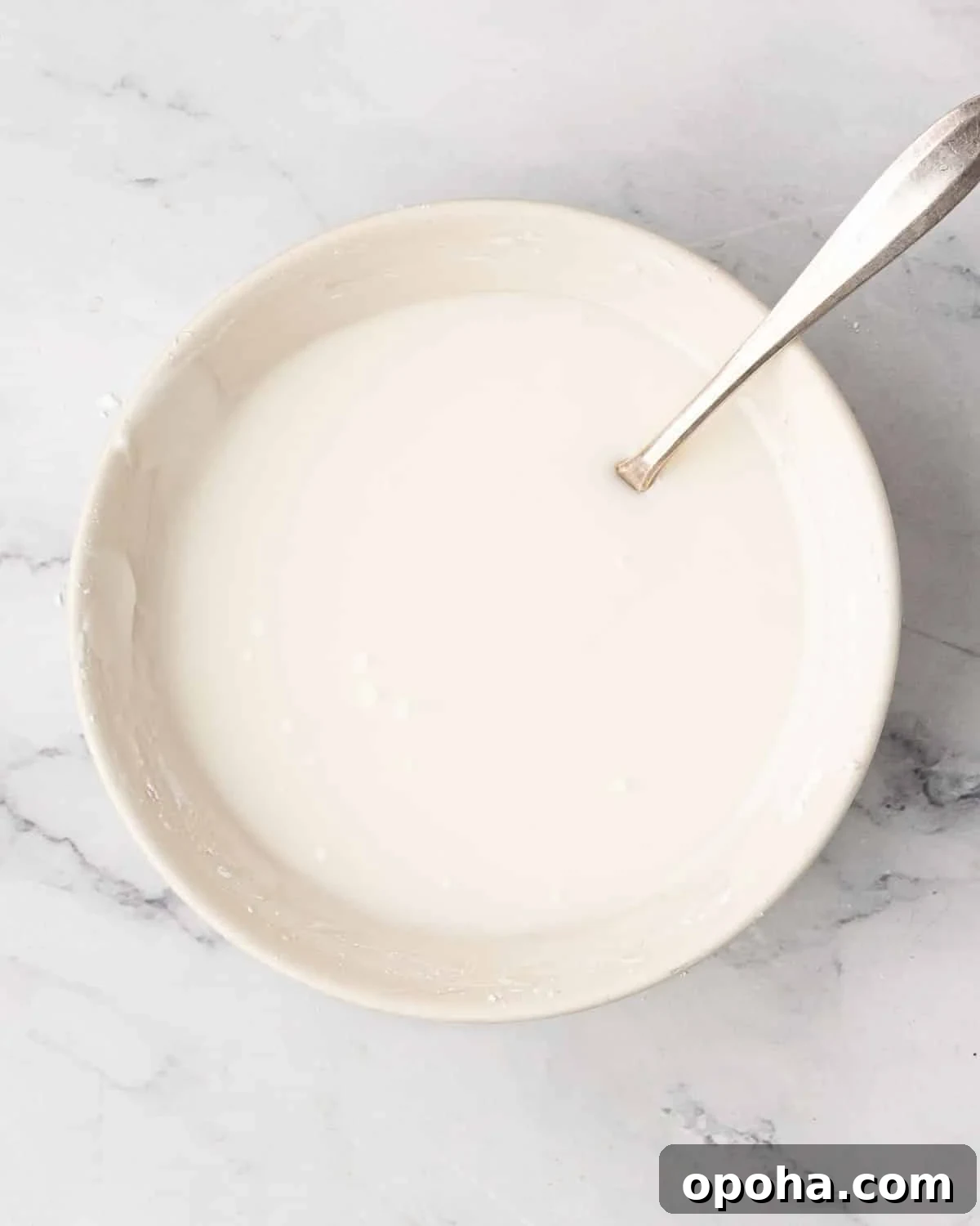 Cherry Pie Bars Recipe: Easy Homemade Cherry Dessert Bars 18 A white bowl with mixed icing and a spoon resting on the side.