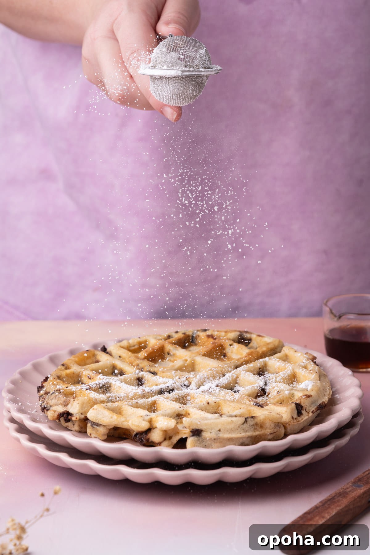 Dusting powdered sugar overtop of waffles with chocolate chips. 