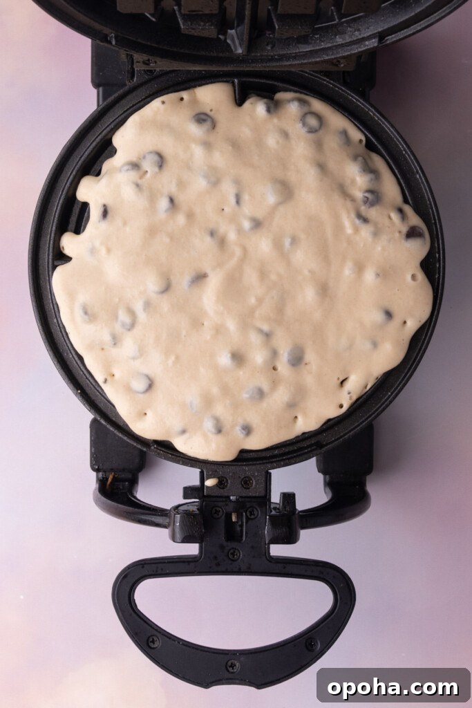 Waffle batter with chocolate chips in a waffle iron before closing the lid to cook.