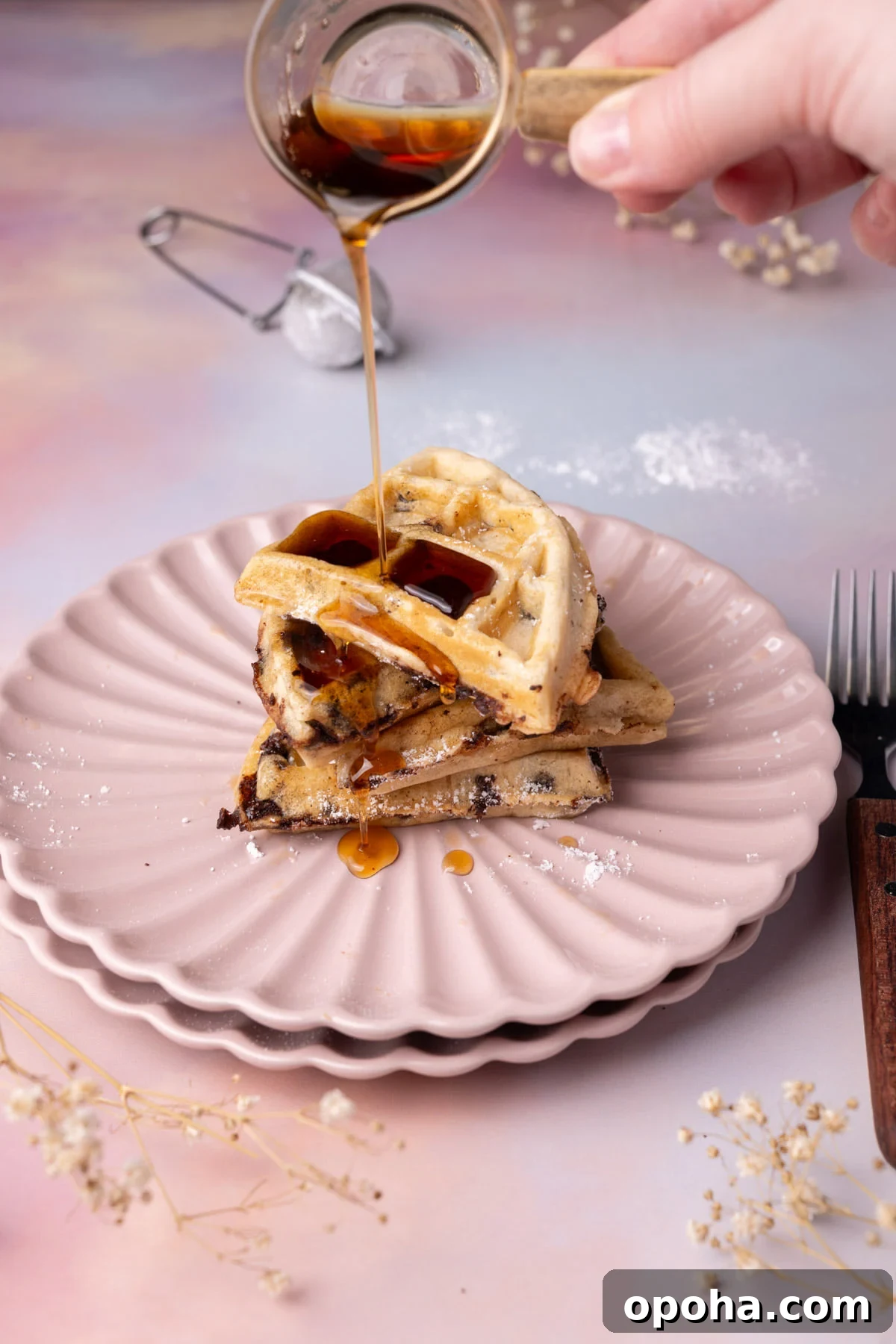 Pouring syrup over 4 quarters of a waffle stacked on top of one another. 
