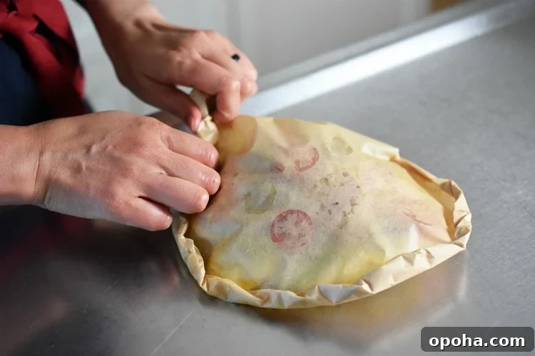 Someone crimping the edges of a Lemon Garlic Chicken Parchment Packet to seal it up.