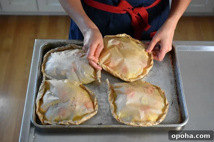 Someone placing the fourth Lemon Garlic Chicken Parchment Packets a rimmed baking sheet.