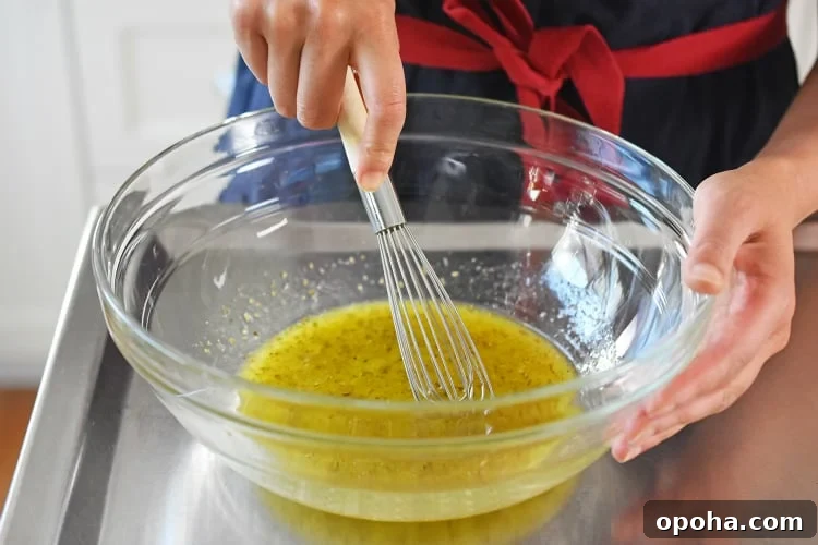 A person is whisking the Lemon Garlic marinade in a glass bowl for Whole30, paleo, and keto chicken foil packets.
