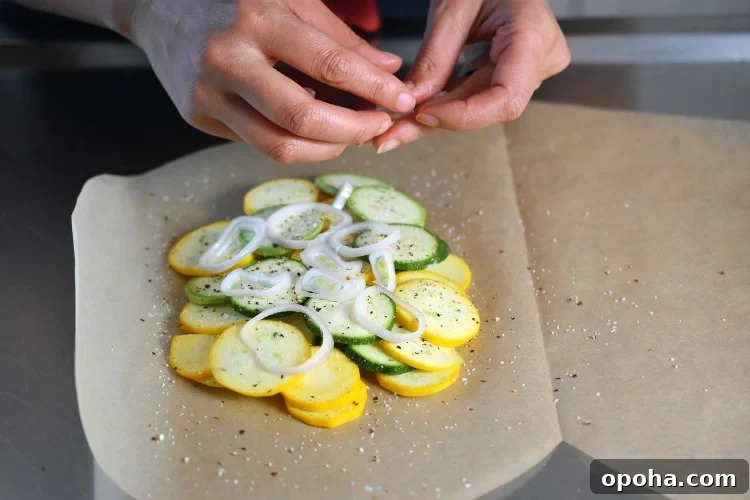 A closeup of a heart-shaped parchment paper with zucchini slices, shallots, salt, and pepper on one half. 