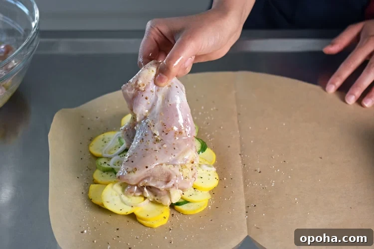 Laying a piece of marinated boneless and skinless chicken thigh on top of the vegetables on a piece of parchment paper. 