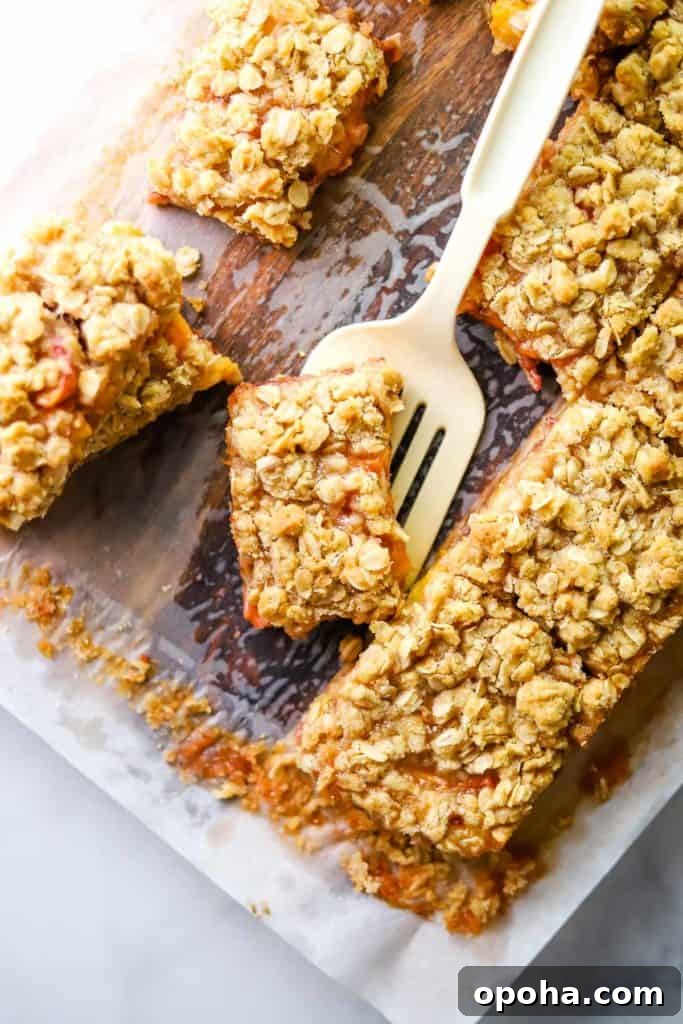 Peach and raspberry oatmeal bars on parchment with a spatula