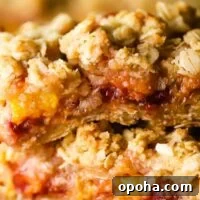 Two peach and raspberry oatmeal bars stacked on top of parchment paper
