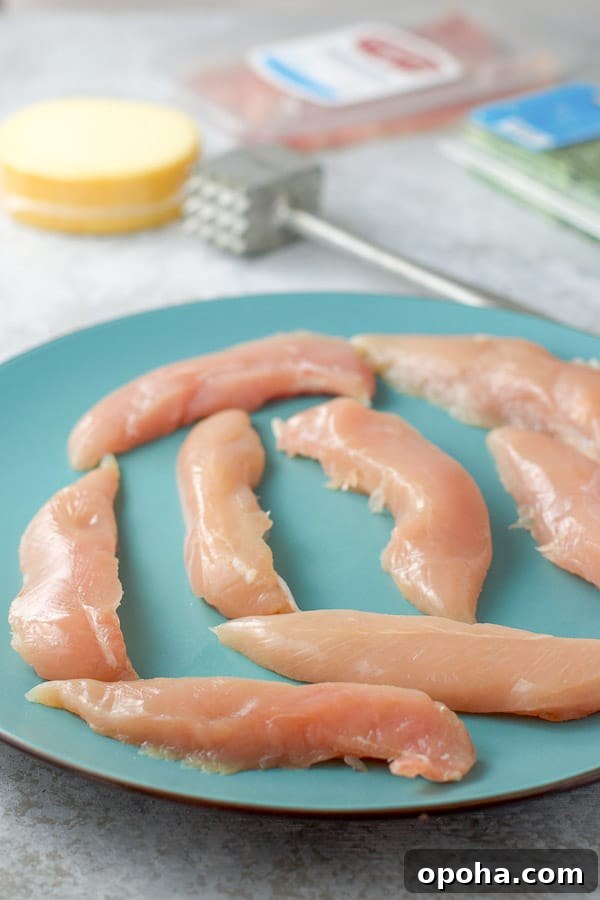 Raw chicken tenders on a blue plate, with gouda cheese, tarragon and meat in the background