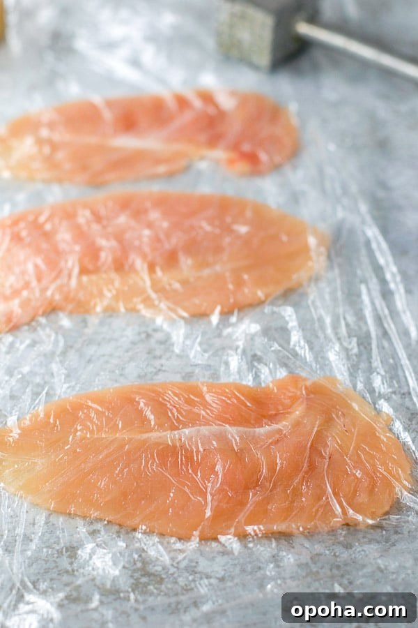 Chicken tenders pounded flat between two plastic wrap sheets
