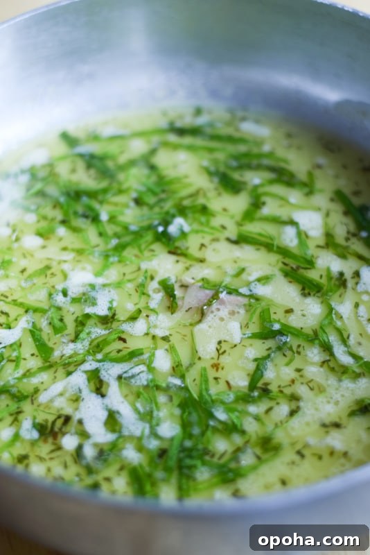 A metal pan with butter sauce and fresh tarragon