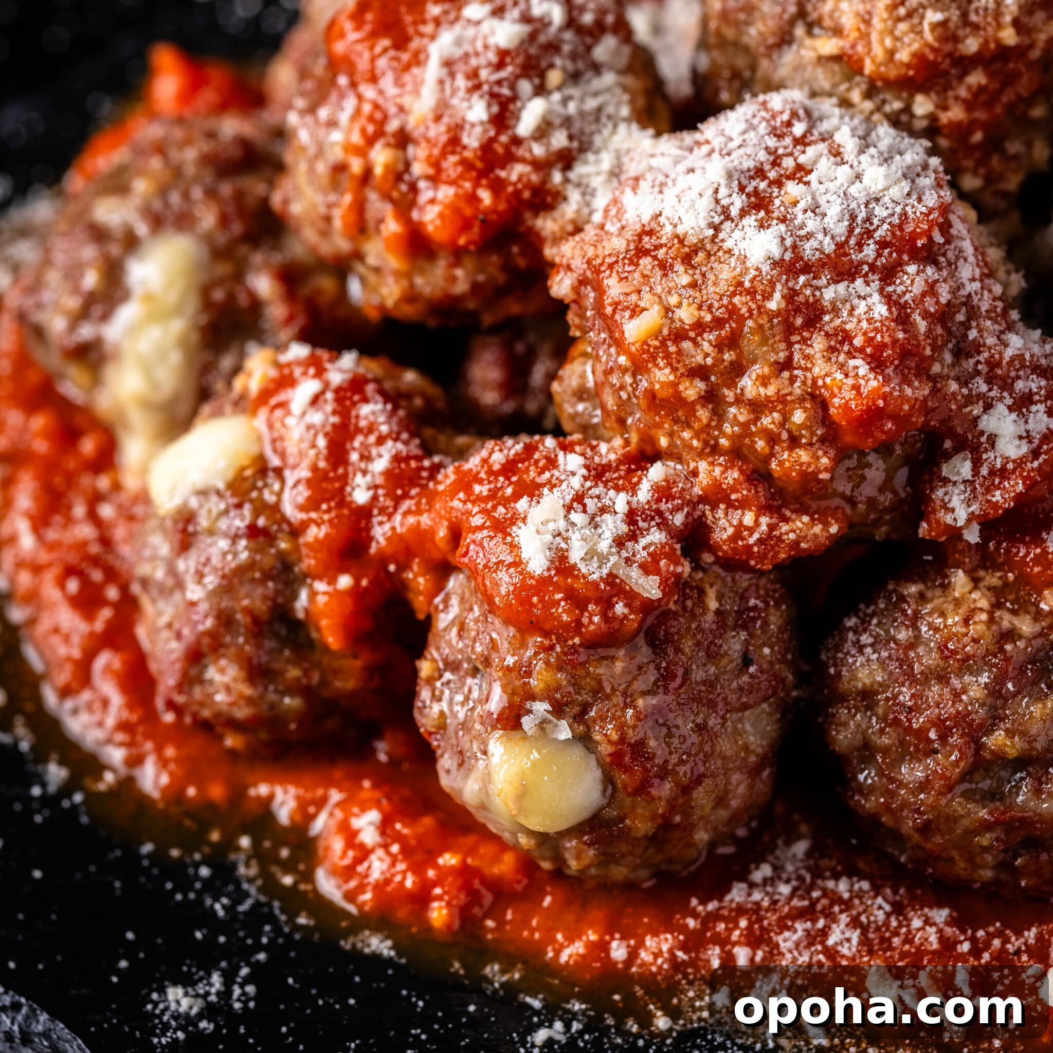 Meatballs dusted with Parmesan cheese on a bed of marinara sauce.