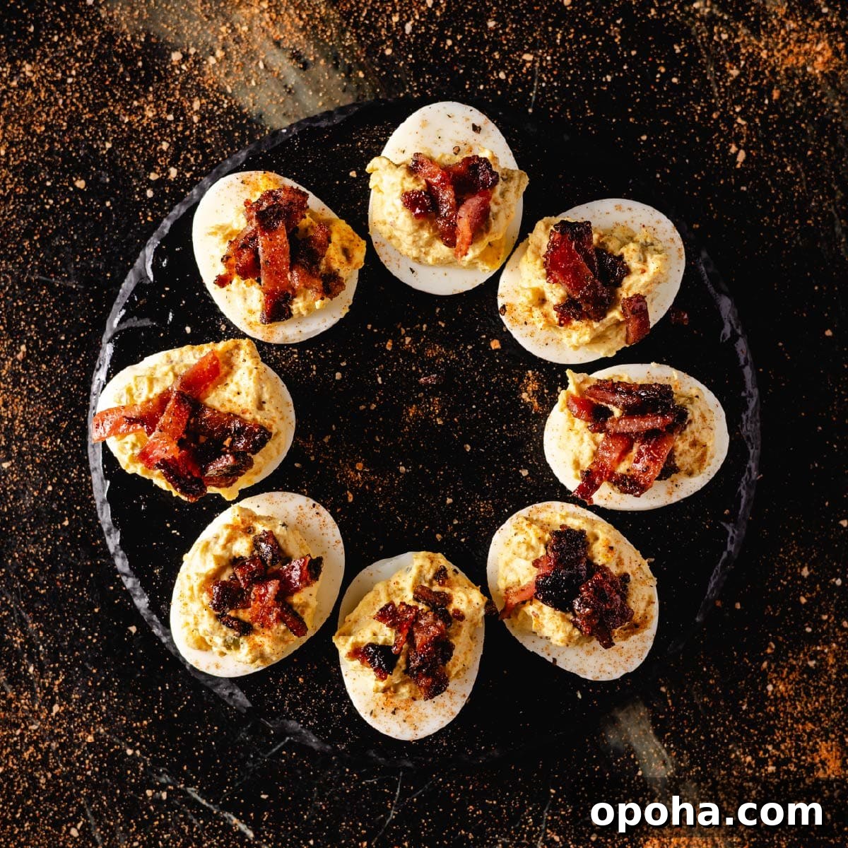 A round, black plate with bacon deviled eggs in a circle.