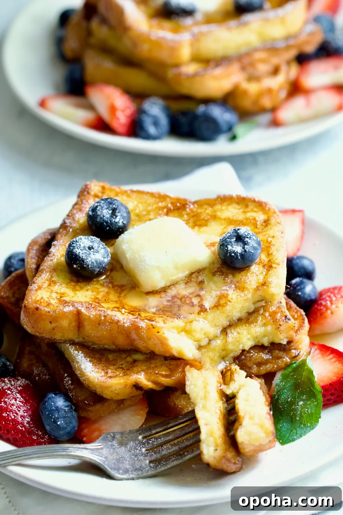 Brioche French Toast on white plate with pat of butter, blueberries and strawberries with two pieces on a fork.
