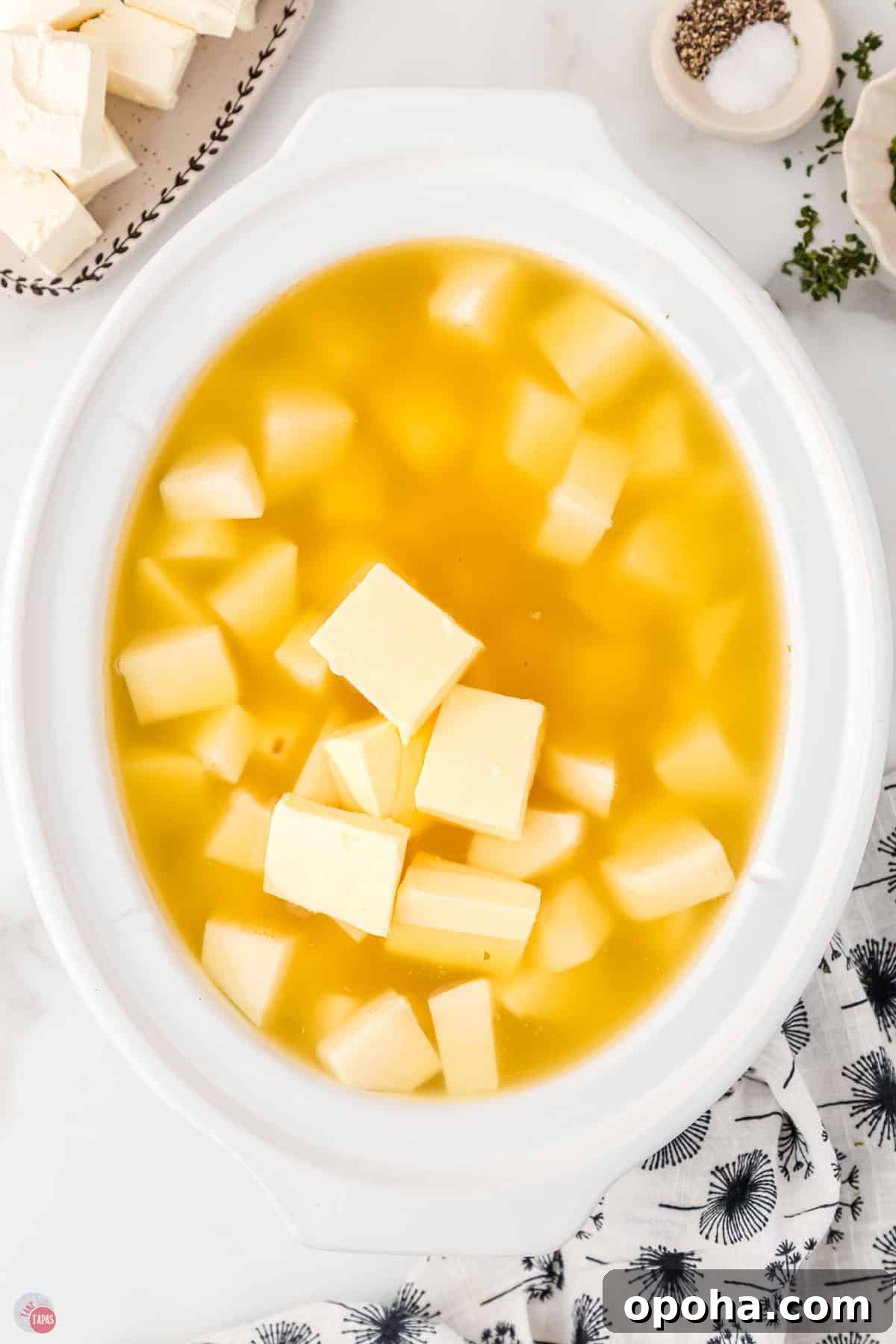 Decadent Million Dollar Mashed Potatoes Recipe 4 diced potatoes and butter covered with broth in a white bowl