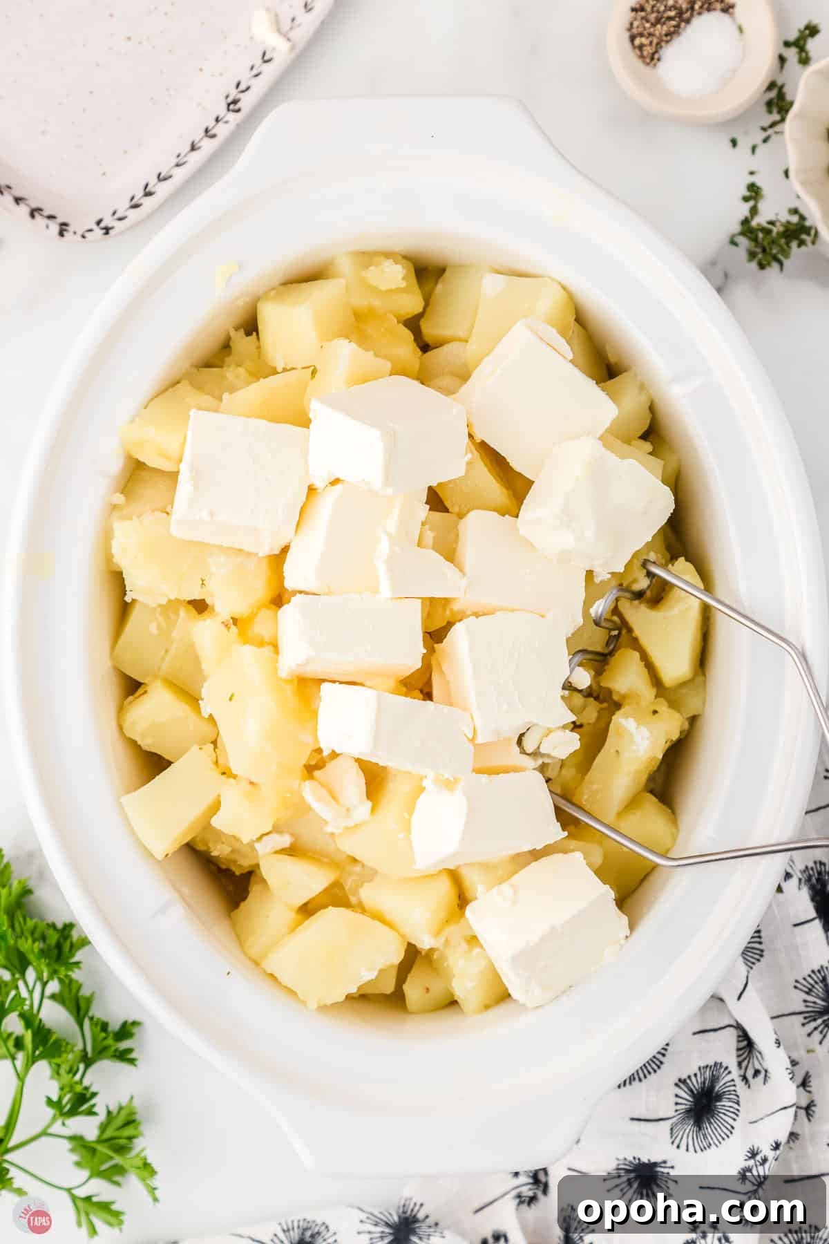 Decadent Million Dollar Mashed Potatoes Recipe 6 white slow cooker filled with diced potatoes and cubes of cream cheese on top