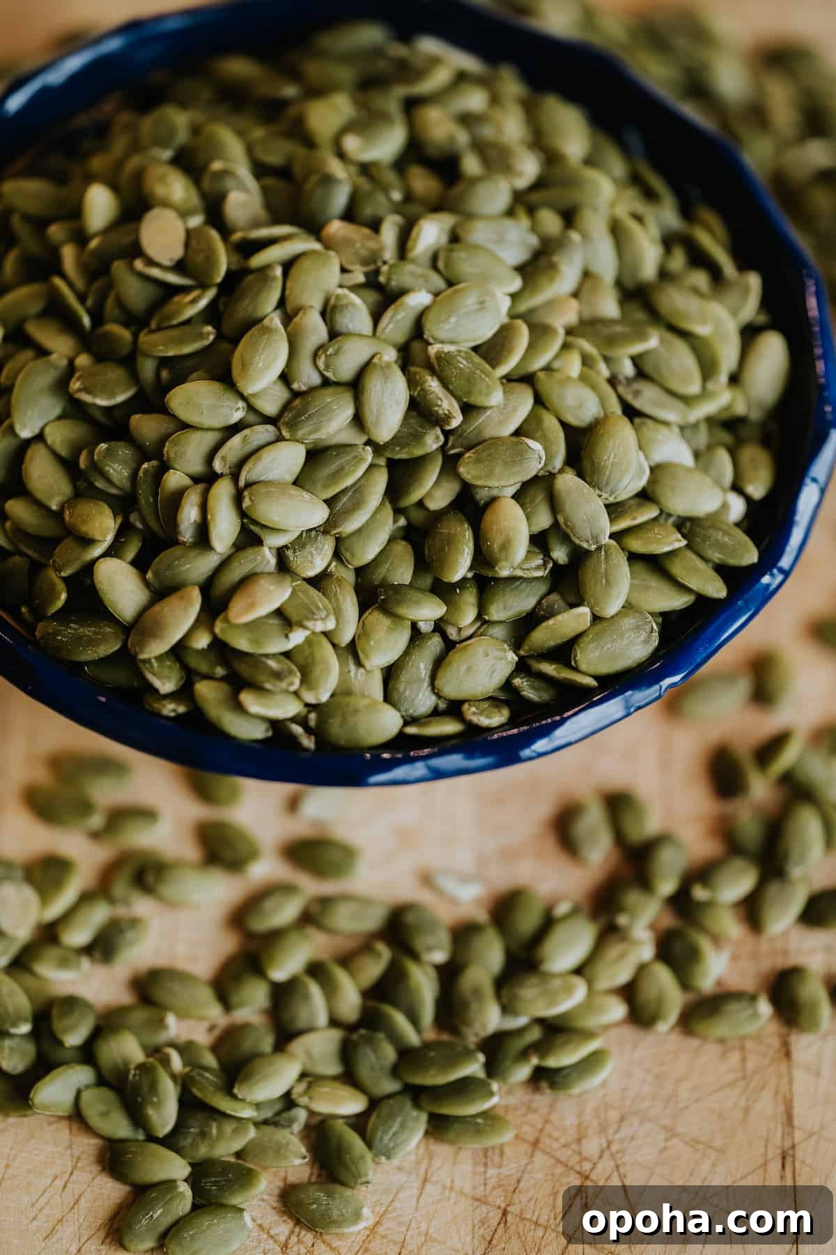 closeup shot of a blue scalloped bowl with raw pepitas on a wooden cutting board.