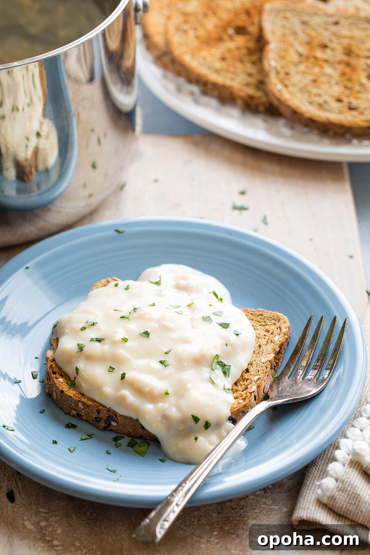"Basic" recipe with creamed tun spooned over a piece of toast on a blue plate with fork; pan and toast sliced in background.