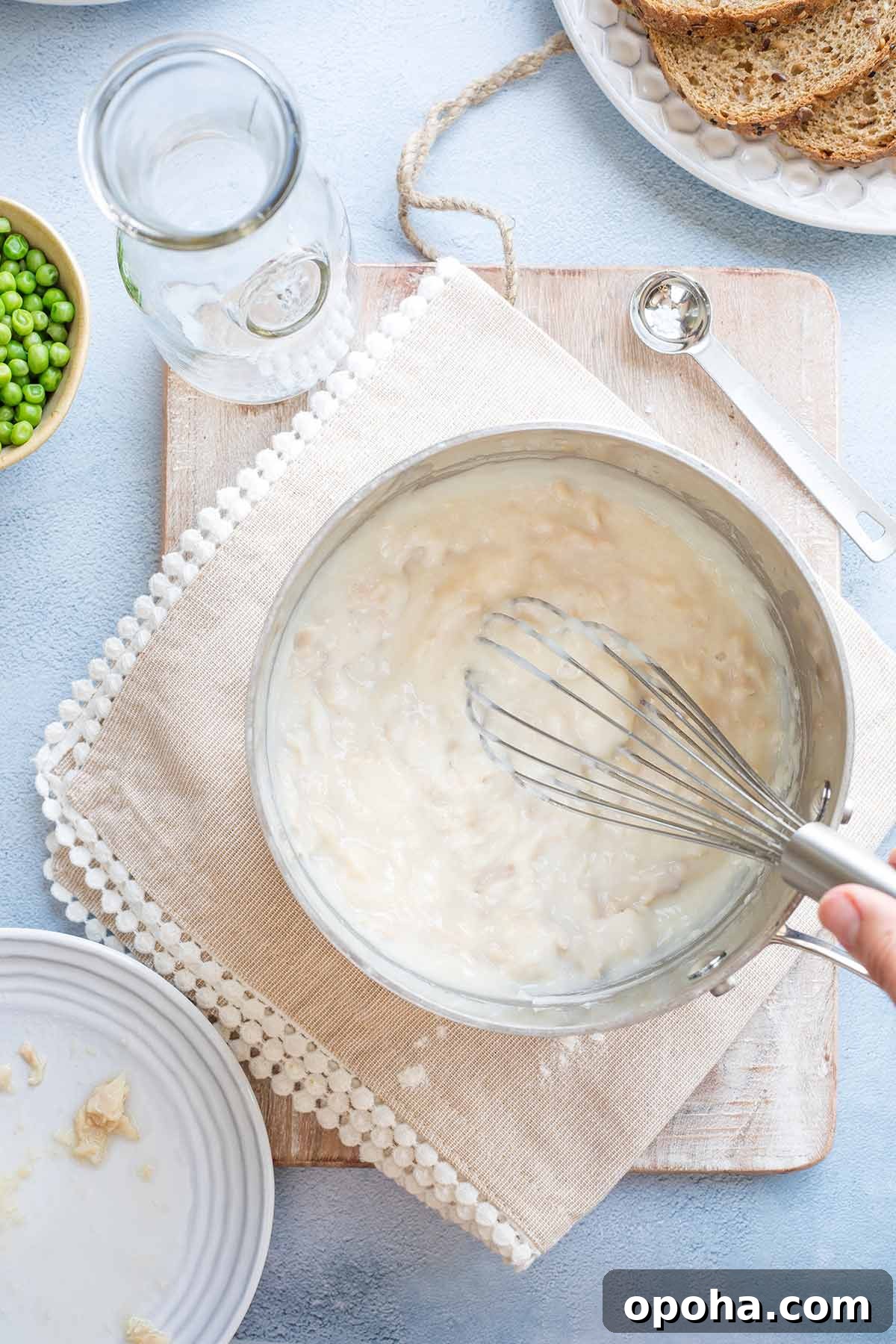 Hand whisking finished creamed tuna sauce in pan.