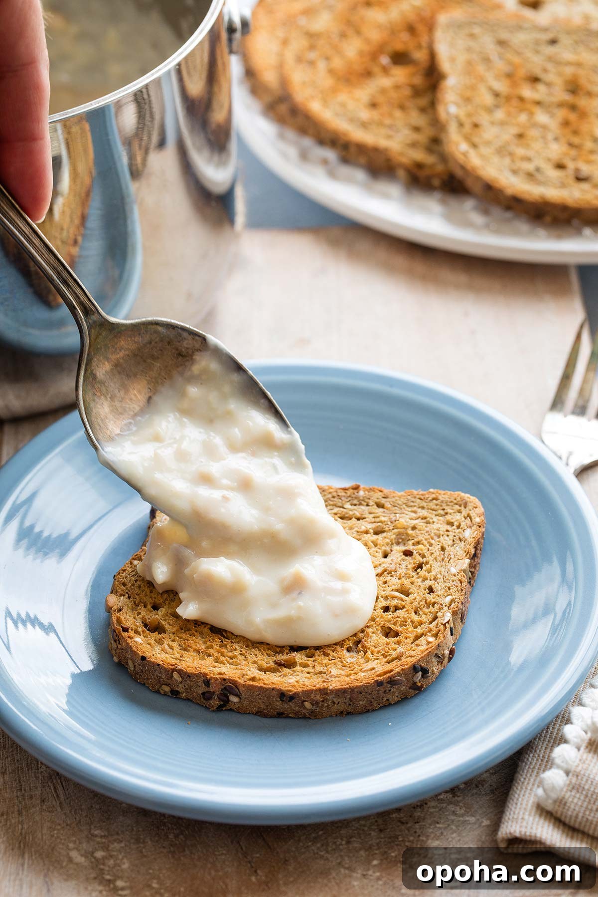 Serving spoon dribbling creamed tuna sauce over a piece of toast on a blue plate.