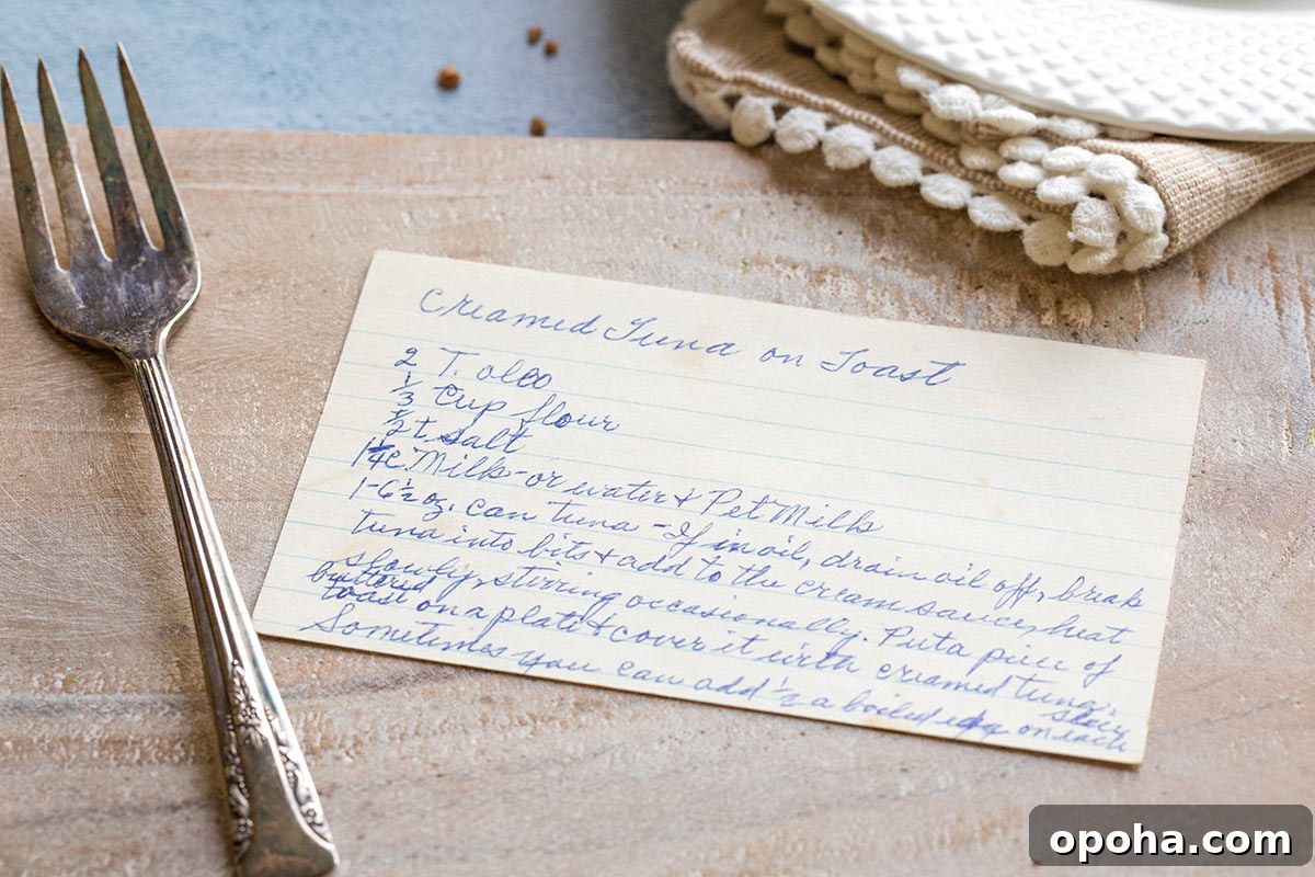 My Grandma's hand-written recipe card for Creamed Tuna on Toast, on a cutting board with fork alongside.