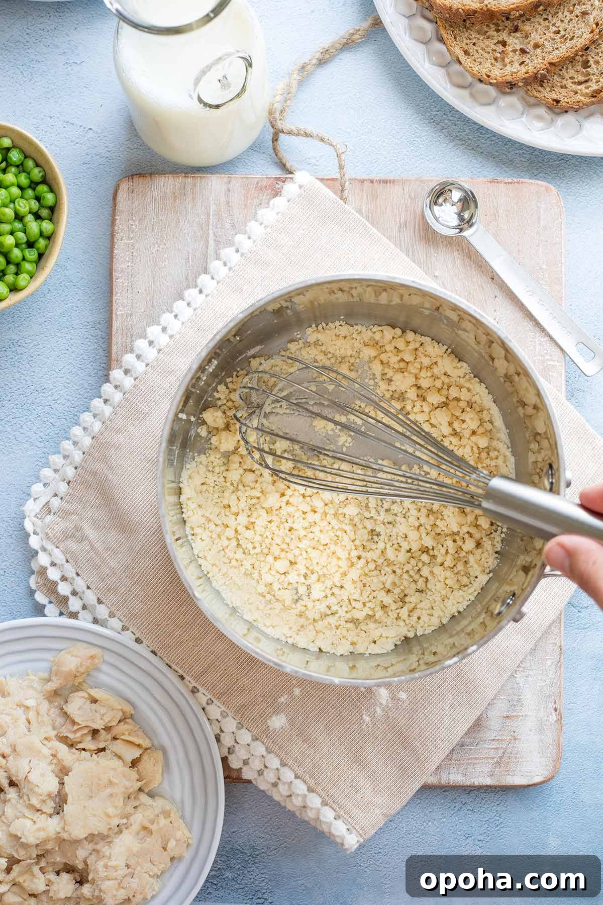 Hand whisking in pan as flour separates into coarse crumbs.