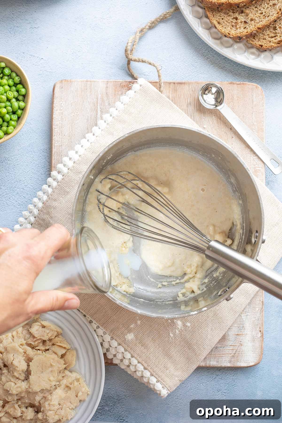 Hand pouring in milk to begin making creamed sauce.