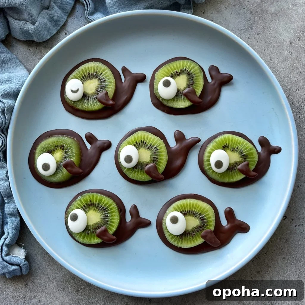 A plate with seven whale bites made from chocolate, slices of kiwi, and candy eyes, arranged neatly on a light blue plate.