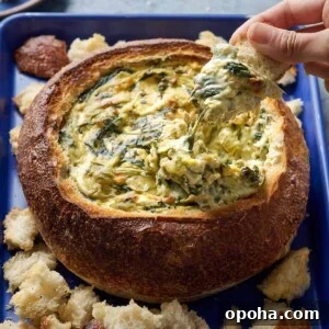 Woman dipping bread into spinach artichoke dip in a bread bowl.