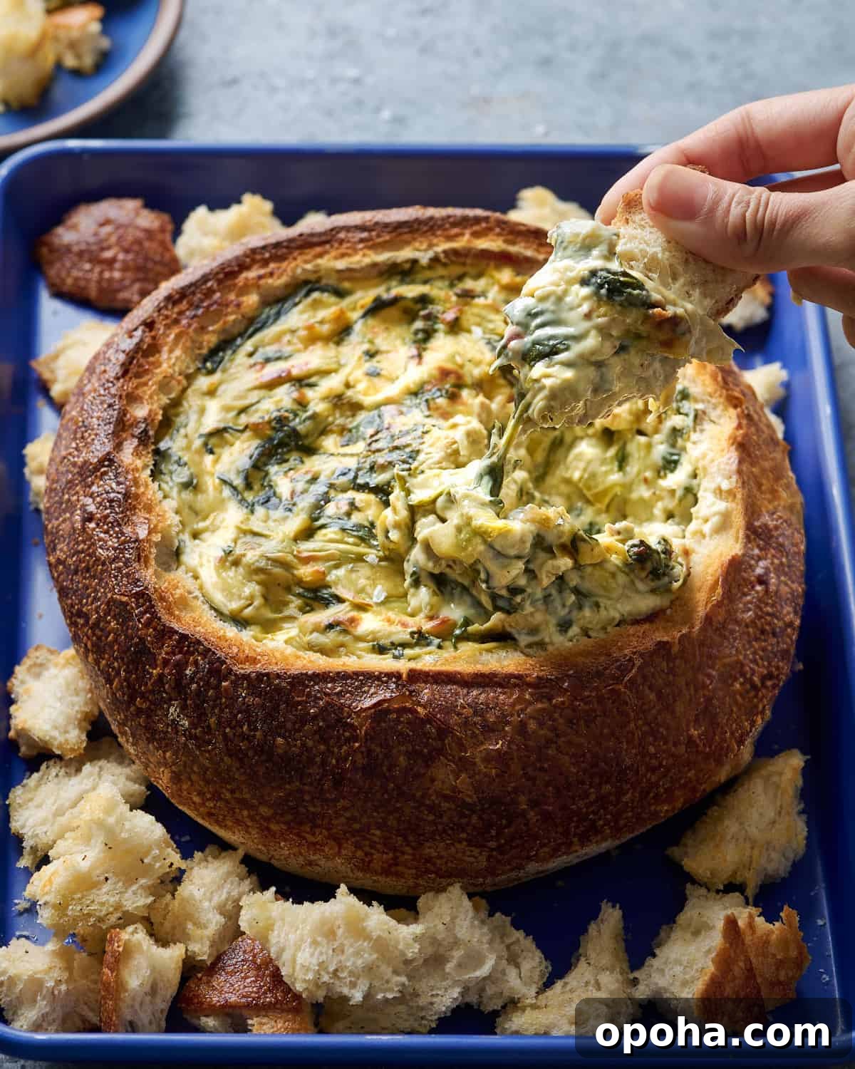 Woman dipping bread into spinach artichoke dip in a bread bowl.
